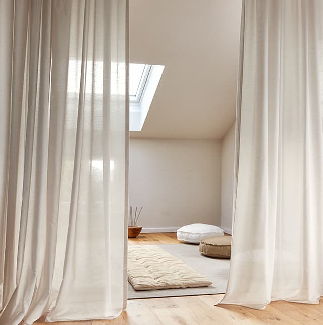 Vorhänge, eine Yogamatte und zwei Poufs in Beigetönen.