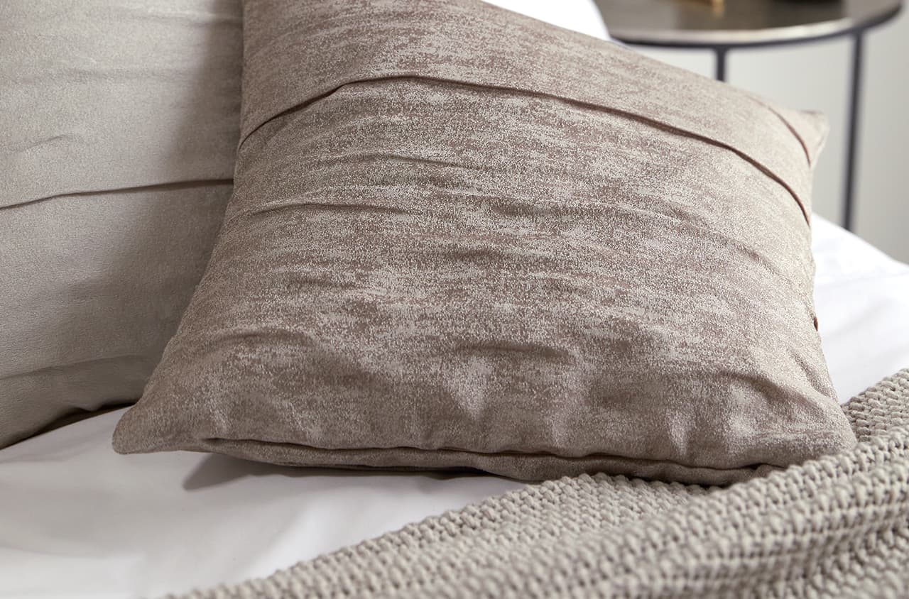 Eine Nahaufnahme von einem beige-braunen Kissen auf einem weißen Bettbezug.
